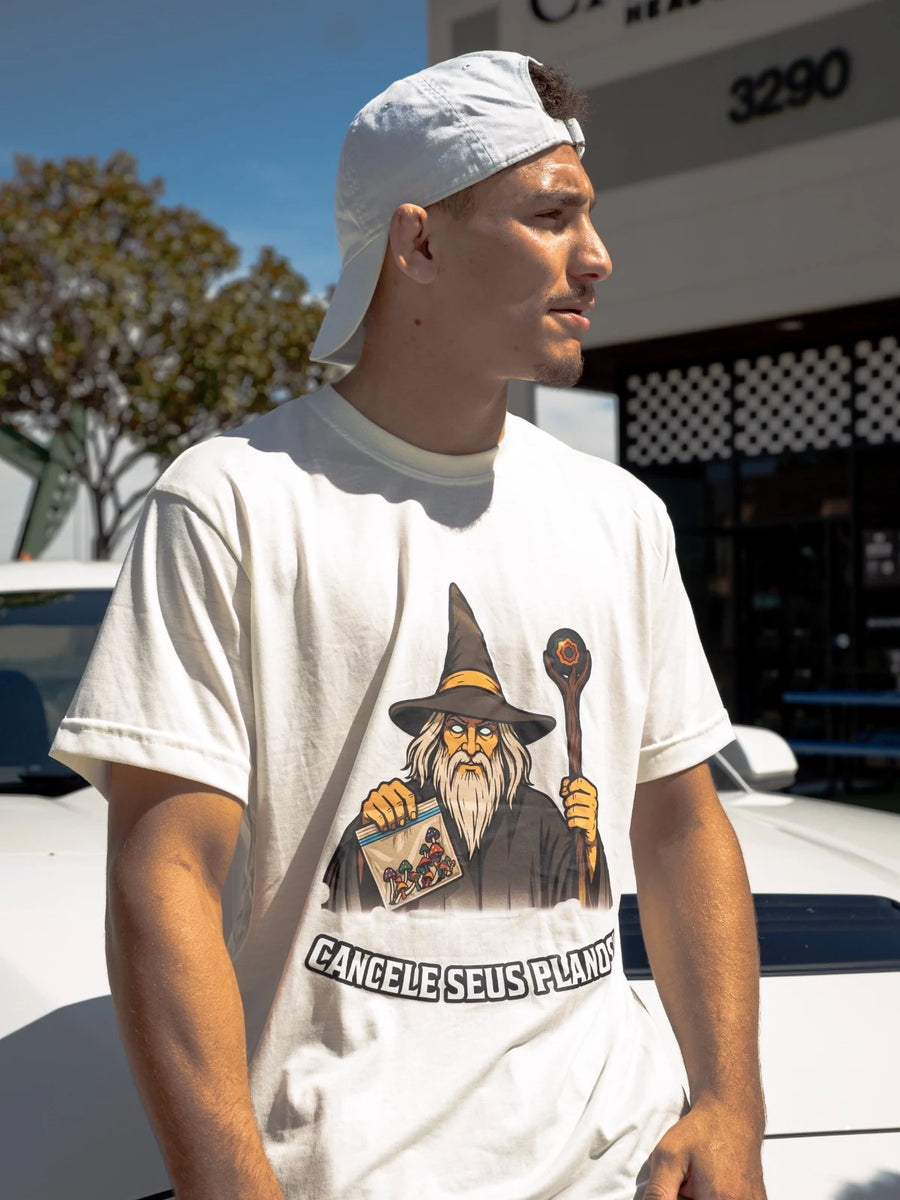 Camiseta creme Cancele Seus Planos no corpo, com estampa de mago, fotografada ao ar livre.